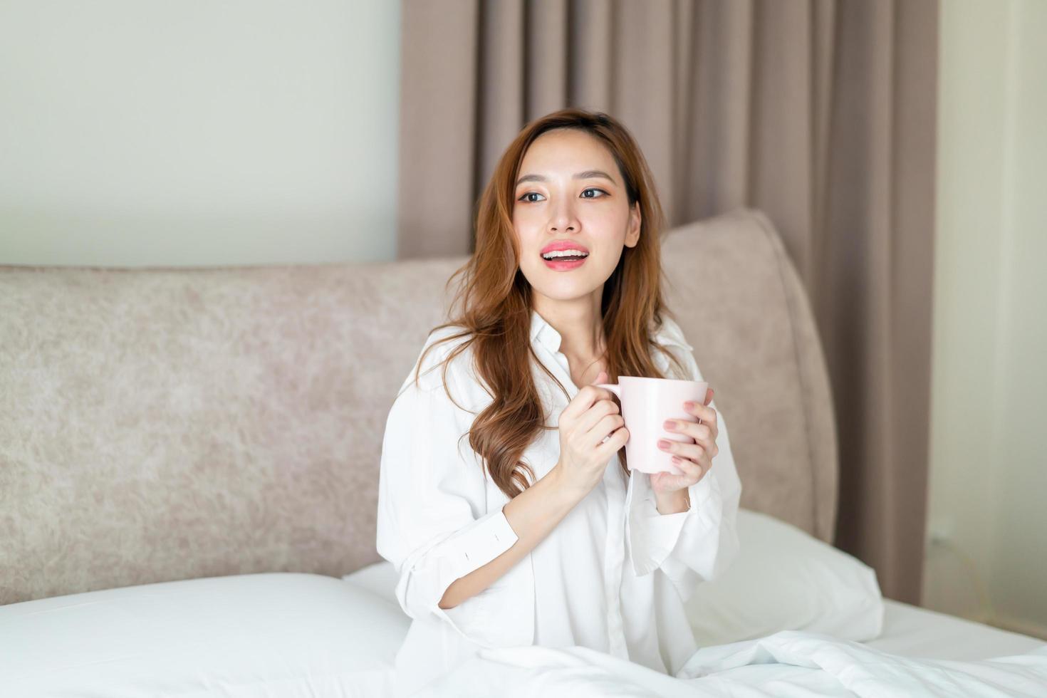 retrato linda mulher asiática acordar e segurando uma xícara de café ou caneca na cama pela manhã foto