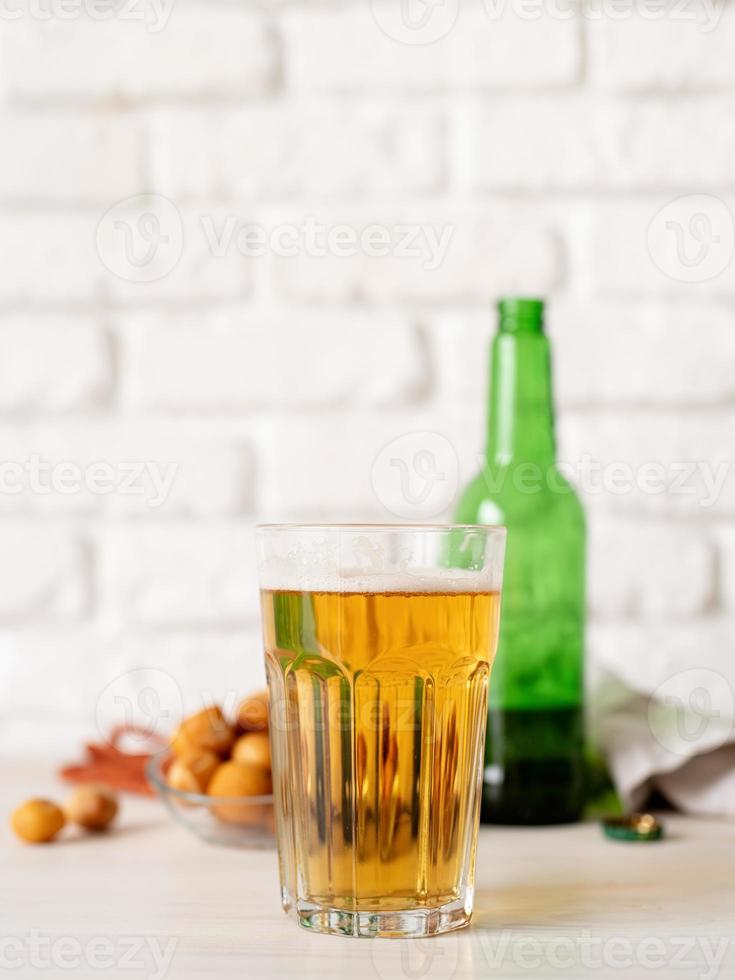 copo cheio de cerveja, garrafa e lanches, fundo de parede de tijolo branco foto