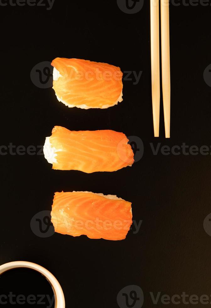 sushi com salmão e pauzinhos isolados no fundo preto foto