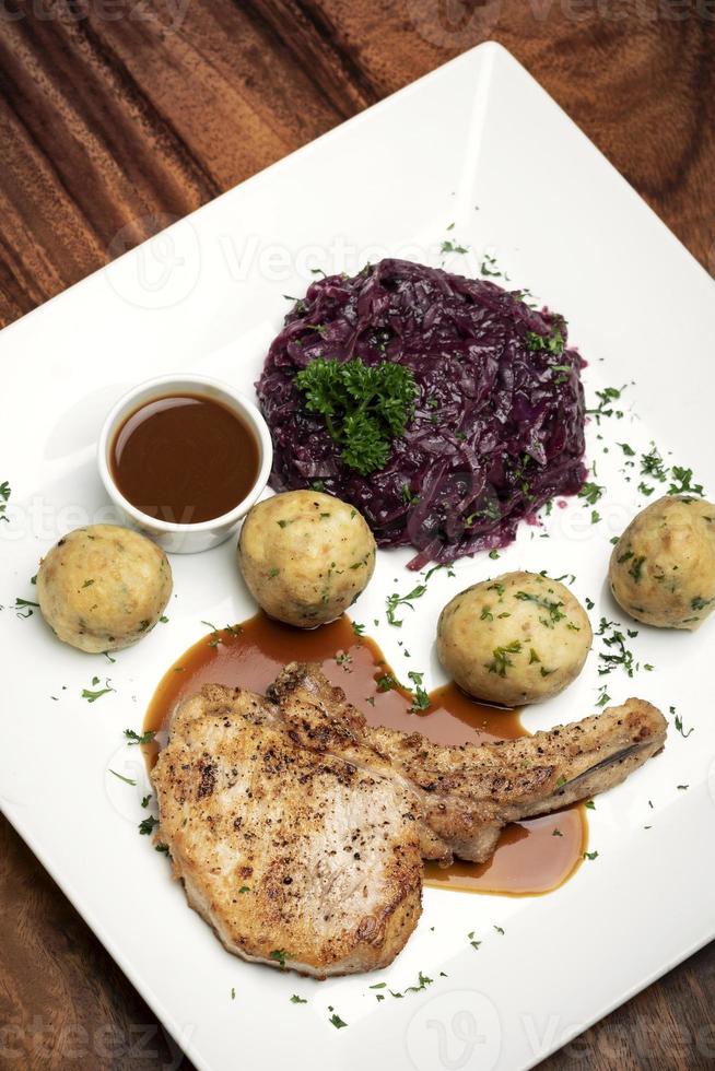 Costeleta de porco grelhada ao estilo alemão com bolinhos de pão e refeição tradicional de couve roxa na mesa de madeira foto