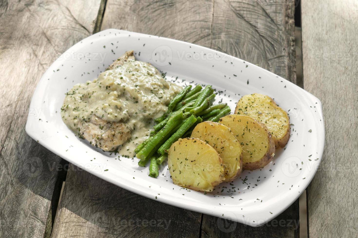 peito de frango com molho de queijo azul e batatas assadas com feijão verde em fundo rústico de madeira velha foto