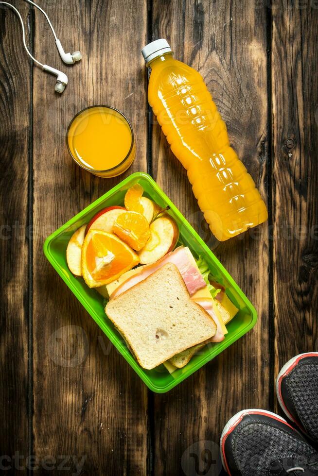 tênis, fones de ouvido, laranja suco , sanduíches e fruta. foto