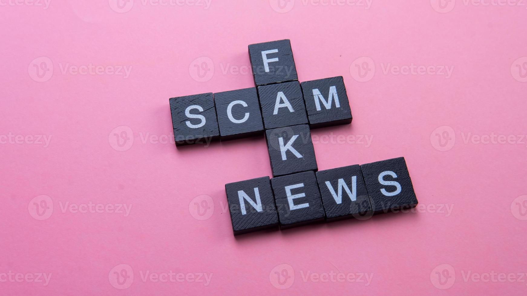 um grupo de ladrilhos de scrabble formando notícias falsas de scam de palavras. foco seletivo nas telhas isoladas em fundo rosa foto