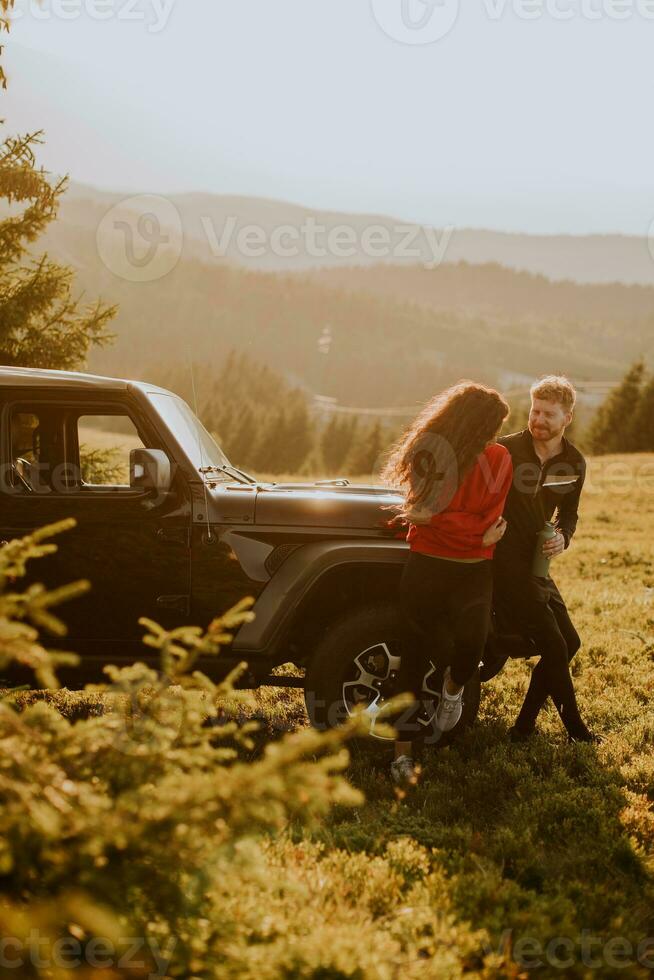 jovem casal relaxando em um capô de veículo de terreno na zona rural foto