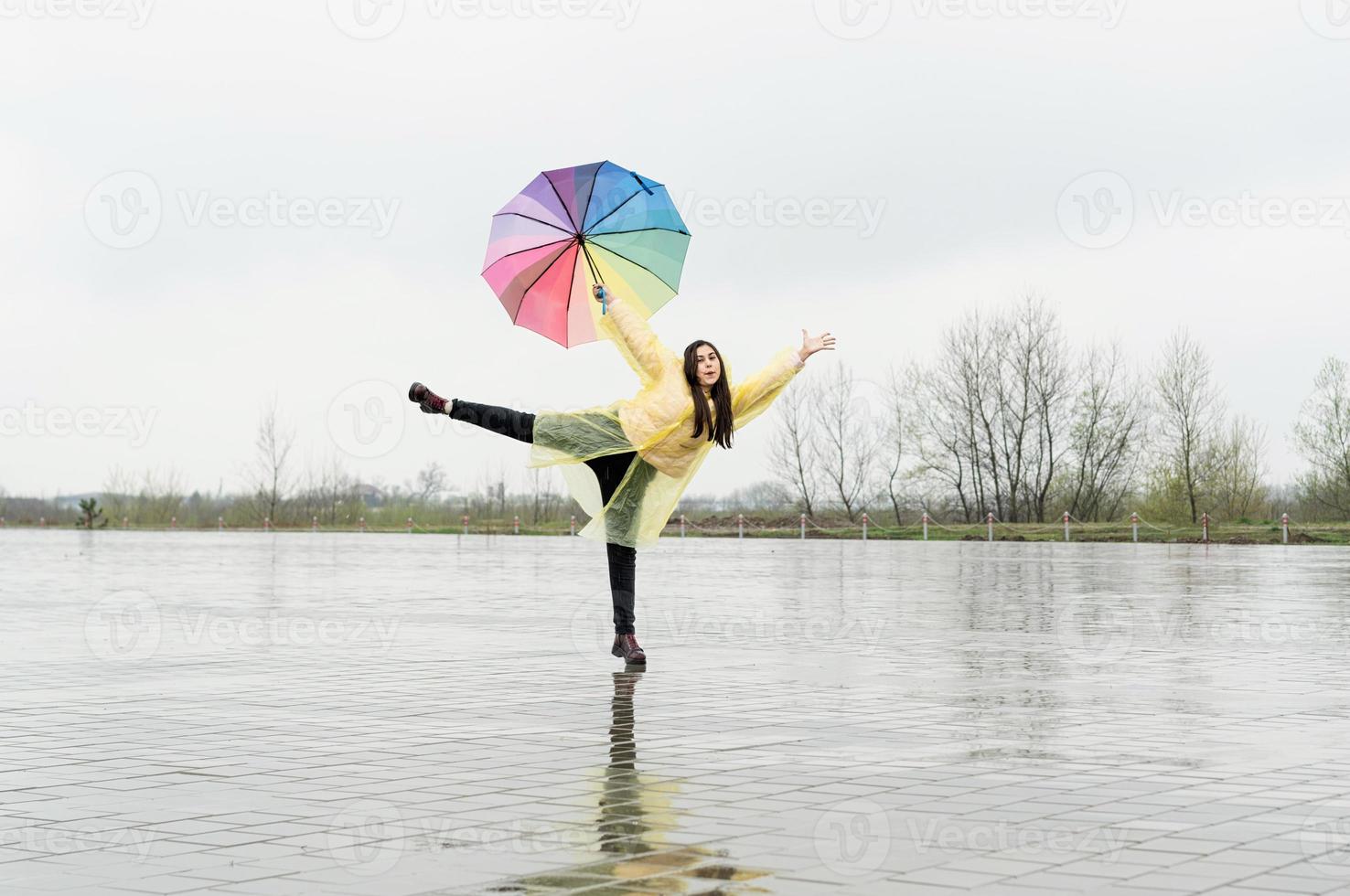 linda mulher morena segurando guarda-chuva colorido dançando na chuva foto