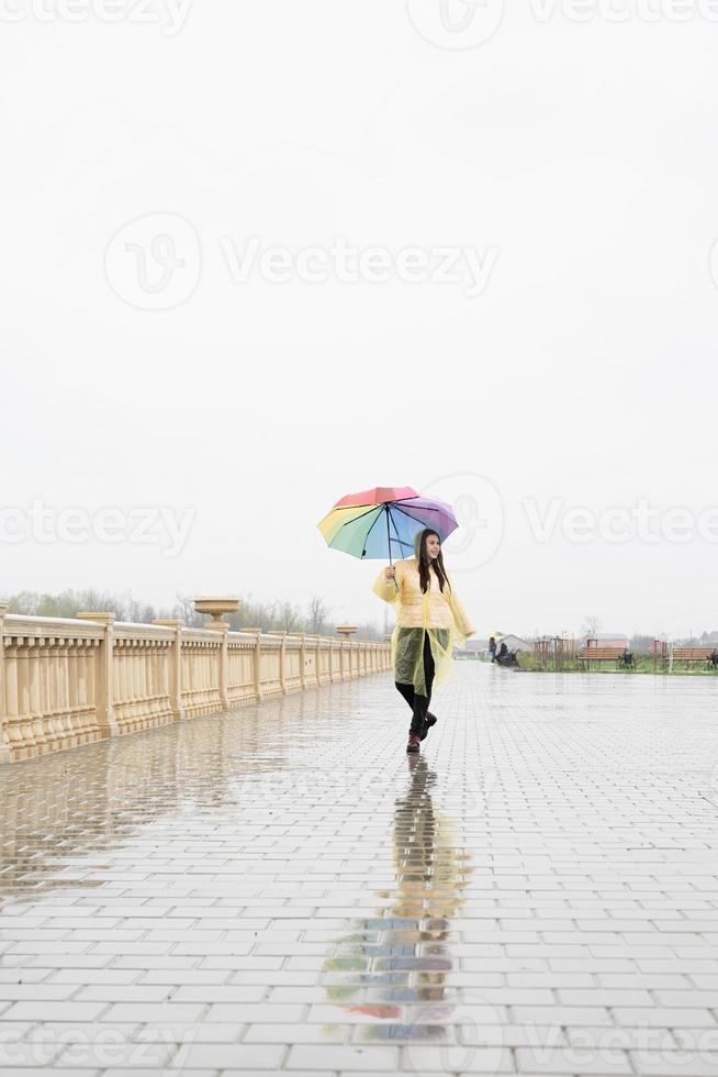 linda mulher morena segurando guarda-chuva colorido andando na chuva foto