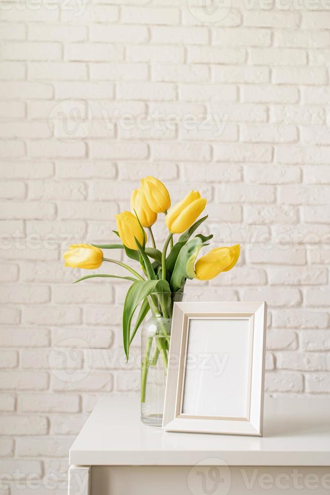 tulipas amarelas em um vaso de vidro e moldura em branco foto