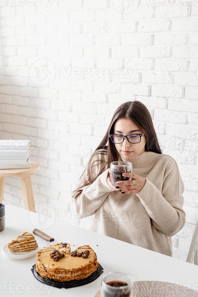 mulher sentada à mesa branca, comendo bolo e tomando café foto