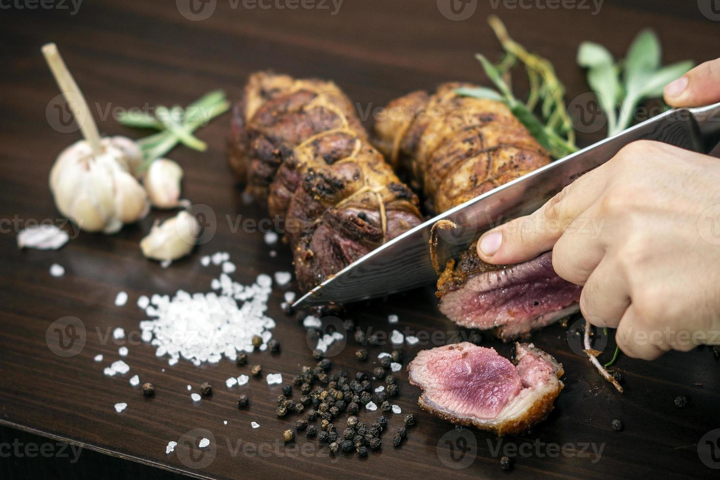 fatiar uma porção de rosbife orgânico com faca na mesa de madeira com alho, pimenta e sal em melbourne, austrália foto