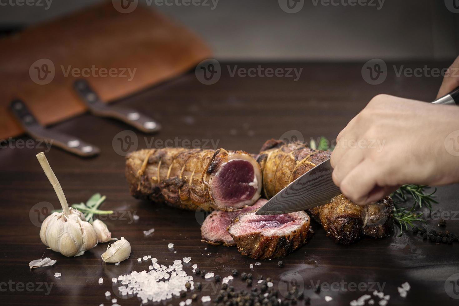 fatiar uma porção de rosbife orgânico com faca na mesa de madeira com alho, pimenta e sal em melbourne, austrália foto