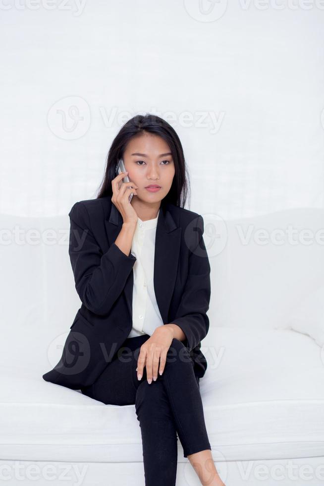 jovem mulher asiática falando de telefone e sorriso na sala de estar. foto