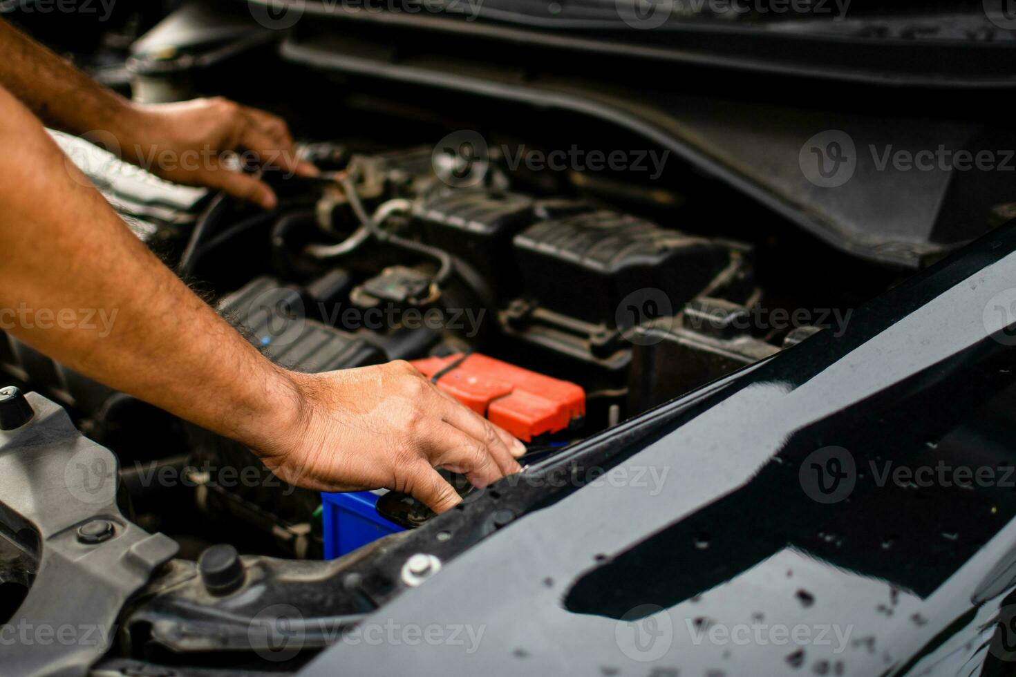 fechar-se, a mãos do uma masculino técnico estão usando uma ferramenta para substituir a carro bateria, estacionado às lar. Preto carro, a bateria é danificado. homem é verificação a bateria do uma Preto carro com não poder. foto