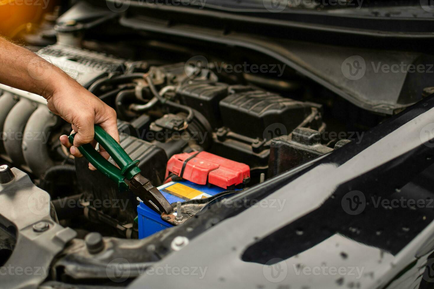 fechar-se, a mãos do uma masculino técnico estão usando uma ferramenta para substituir a carro bateria, estacionado às lar. Preto carro, a bateria é danificado. Ferramentas ter alicate e chaves de fenda. foto