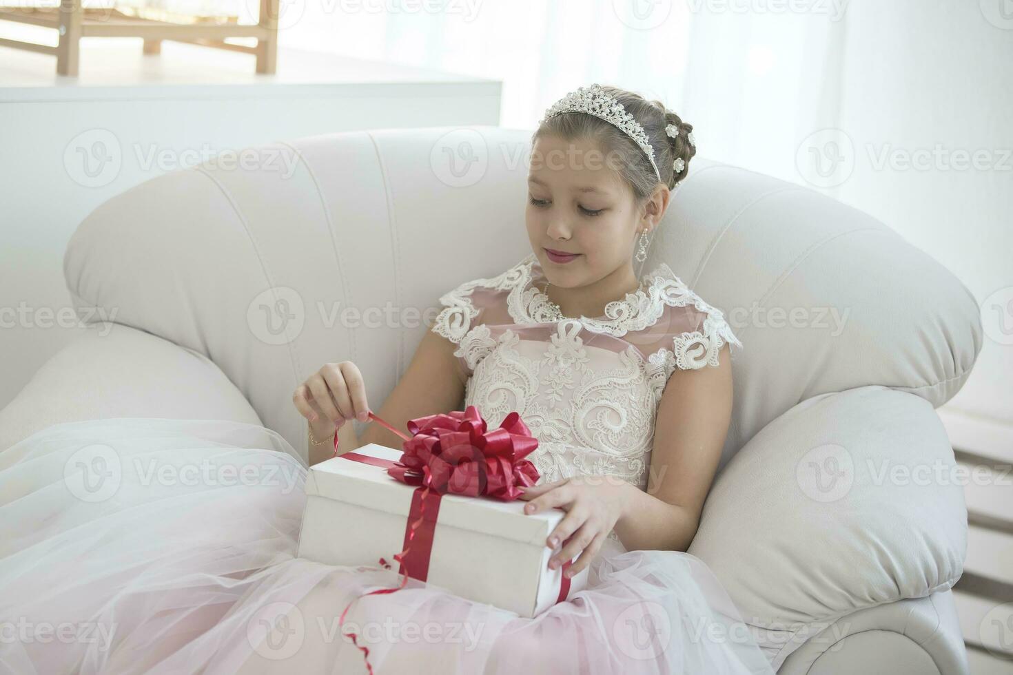 elegante menina abre uma presente.menina do dez anos velho com uma presente caixa dentro uma branco cadeira foto