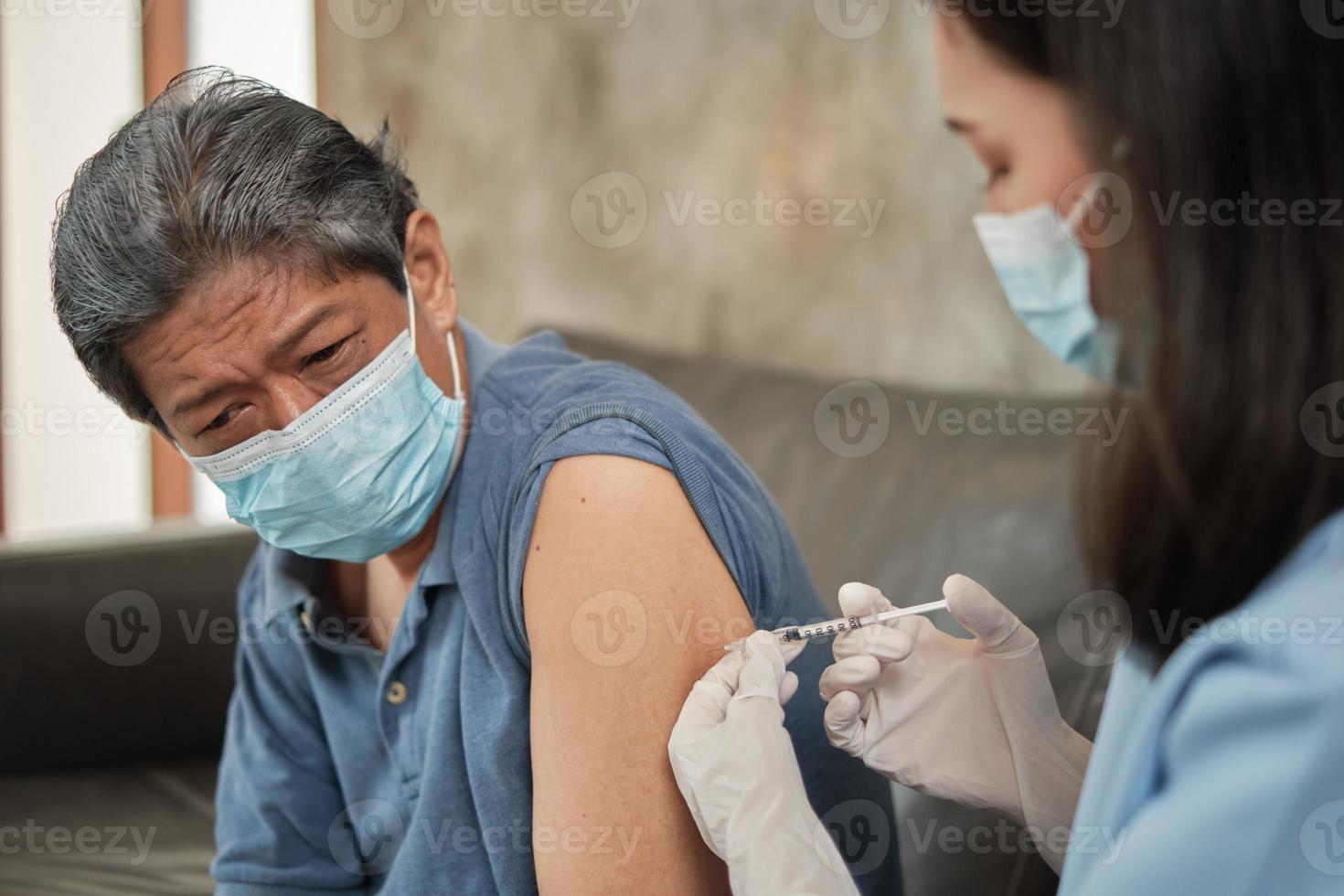 uma médica asiática está vacinando um homem idoso em casa. foto