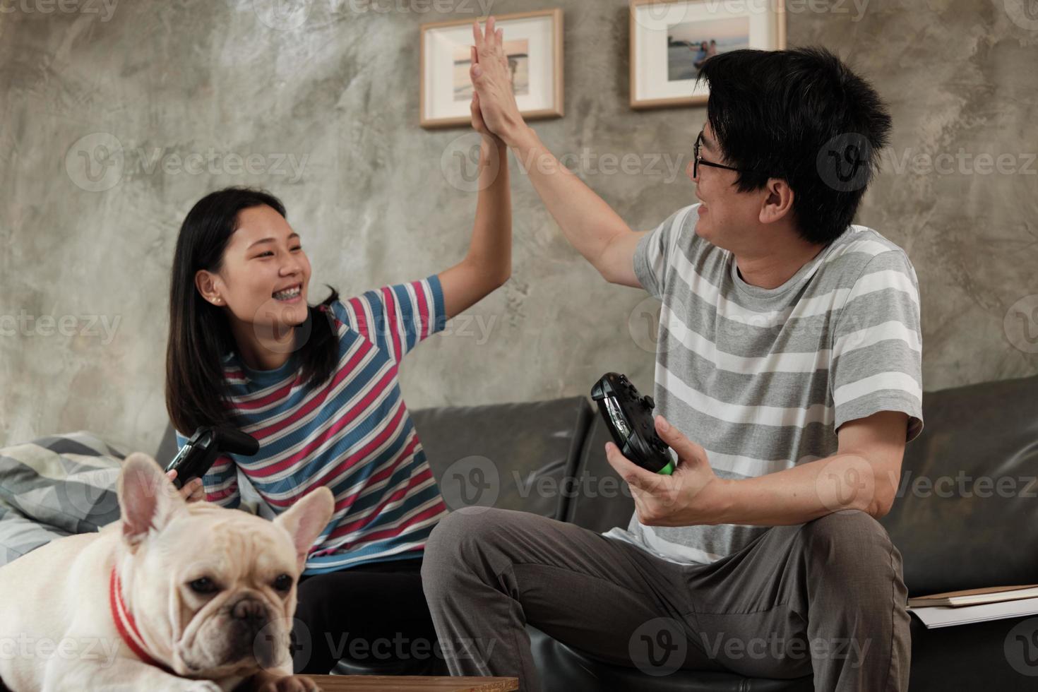 casal asiático está jogando videogame e cachorro de estimação nas proximidades. foto