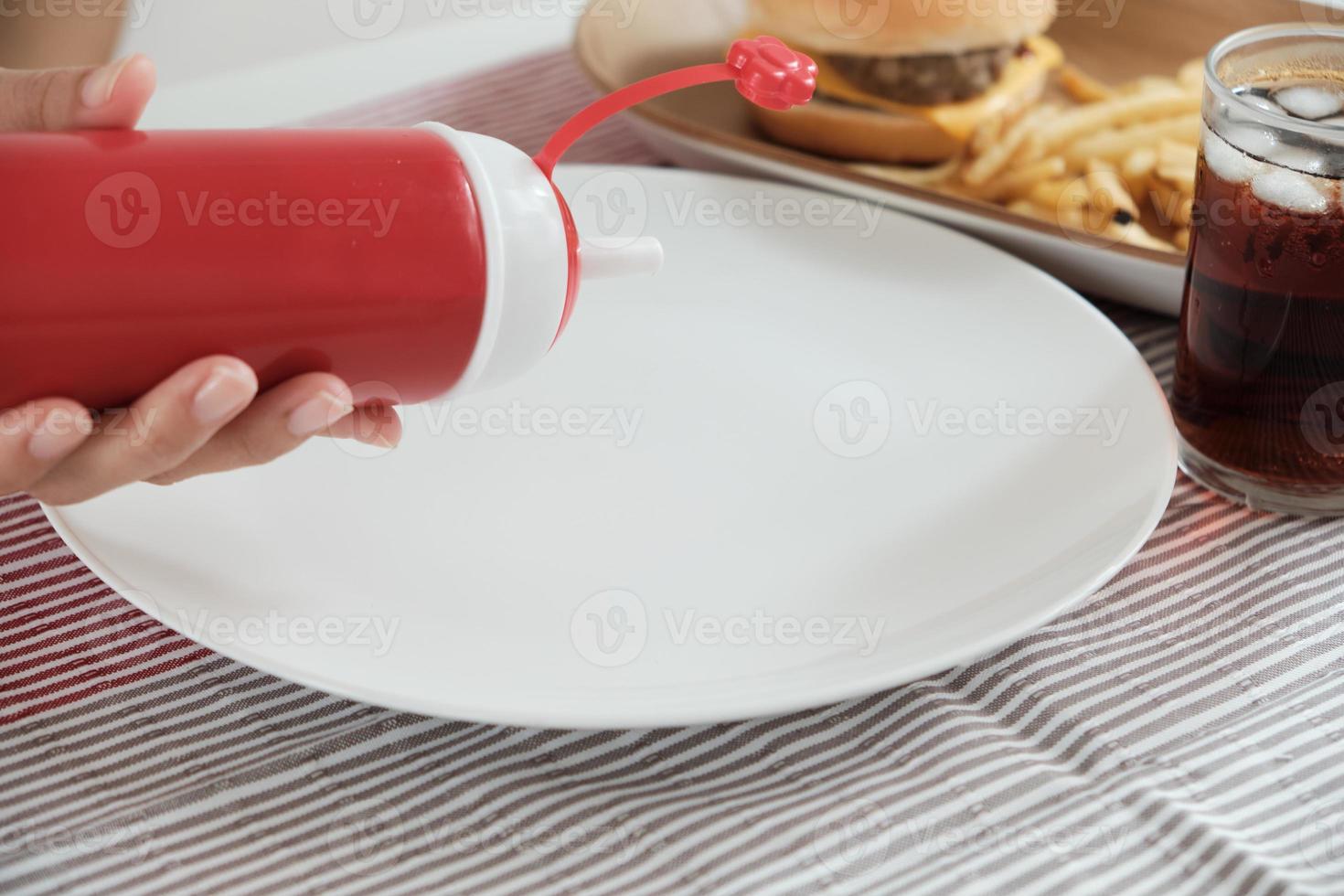 despejando ketchup de garrafa vermelha em um prato branco vazio. foto