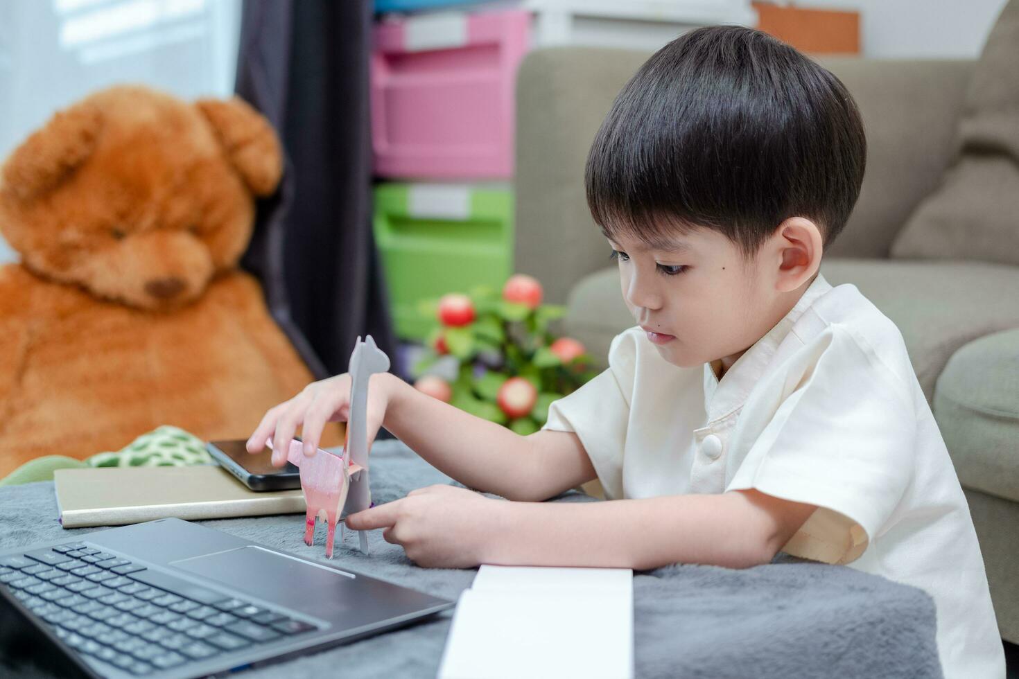 ásia Garoto estudando conectados em computador portátil e Aprendendo a partir de papel animais foto