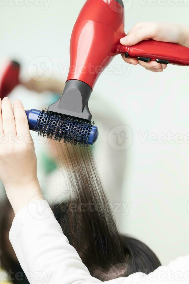 mãos do estilista de cabelo secagem morena cabelo do cliente usando secador de cabelo e pente dentro beleza salão foto
