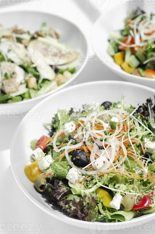 Mistura de saladas orgânicas frescas em tigelas na mesa branca do restaurante foto