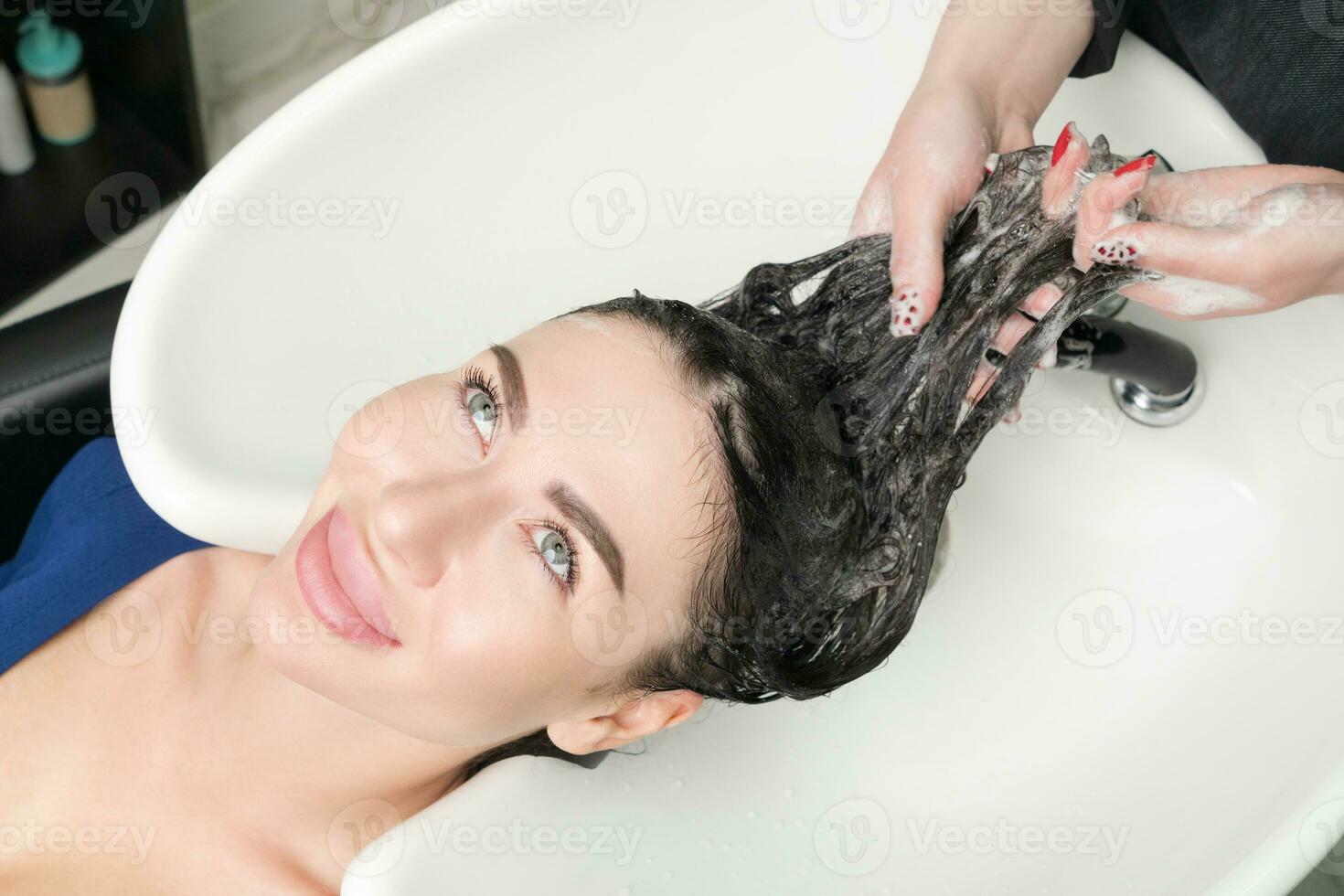 Cabeleireiros mãos lavar grandes cabelo do morena mulher com xampu dentro especial Pia para lavagem foto