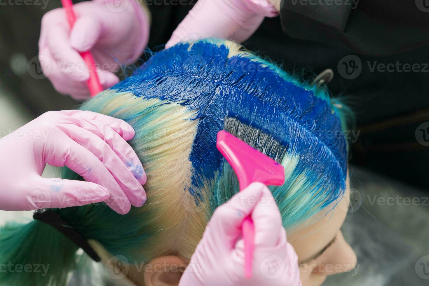 dois cabeleireiro usando Rosa escova enquanto aplicando azul pintura para cliente durante processo do tingimento dela cabelo dentro único cor foto