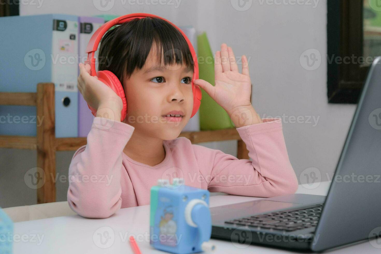 fofa elementar escola menina vestindo fones de ouvido e usando uma computador portátil computador. feliz ásia crianças estude conectados interativamente com computador portátil computador ou Educação escolar em casa, ouvindo para música ou jogando jogos. foto