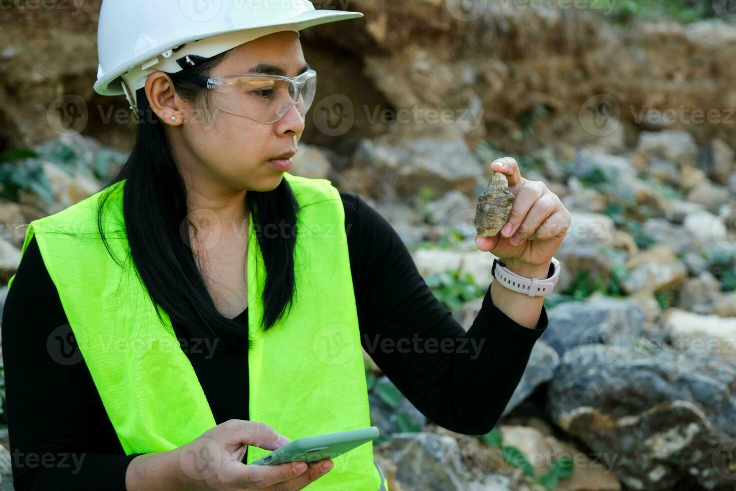 geóloga feminina usando telefone celular para gravar dados analisando rochas ou cascalho. pesquisadores coletam amostras de materiais biológicos. pesquisa ambiental e ecológica. foto