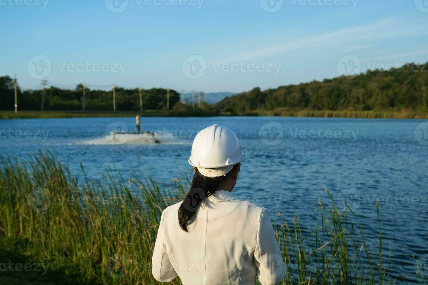 de Meio Ambiente engenheiro vestindo uma branco capacete usa uma Móvel telefone para operar a oxigênio turbina arejador dentro uma lago. água e ecologia conceito. foto