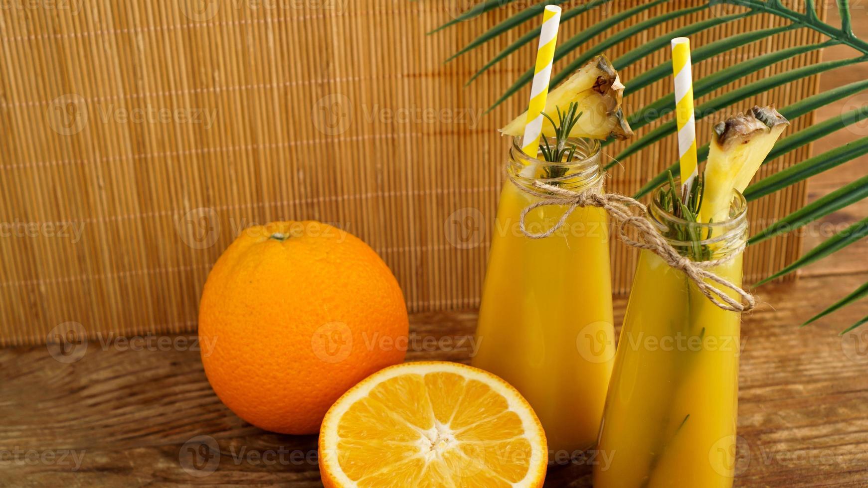 duas garrafas de suco tropical com canudos de papel. laranjas e abacaxi foto