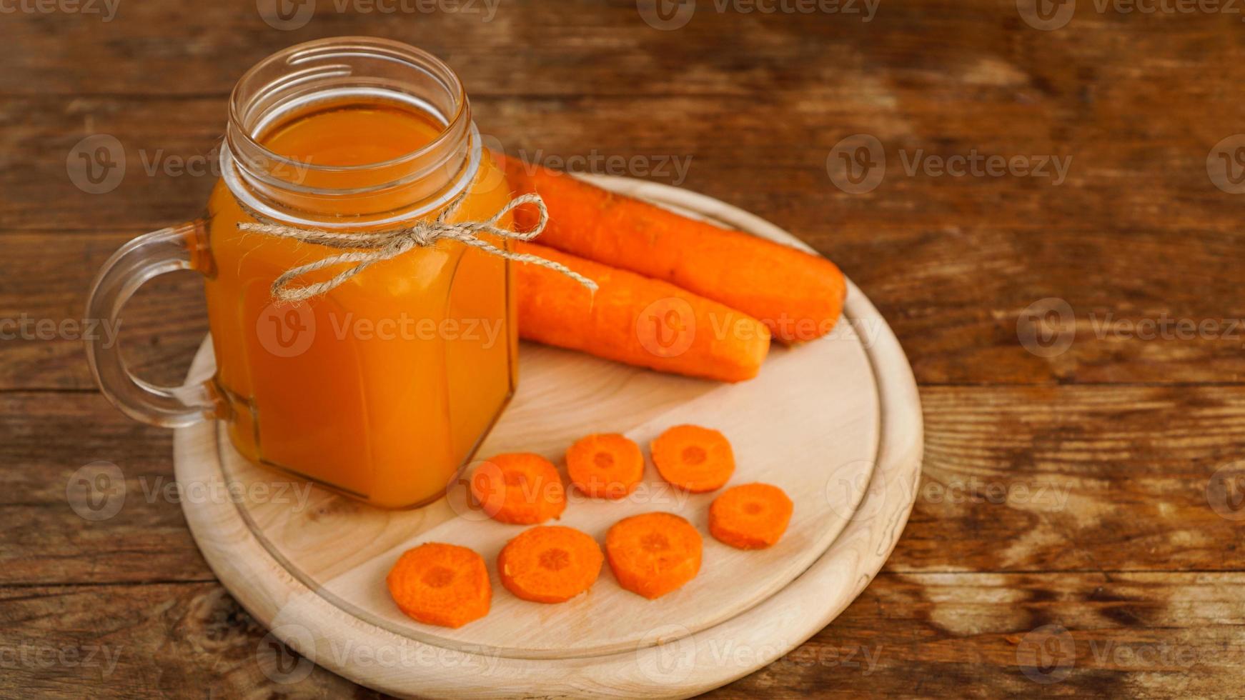 Suco de cenoura de laranja brilhante em uma jarra de vidro com fundo de madeira foto