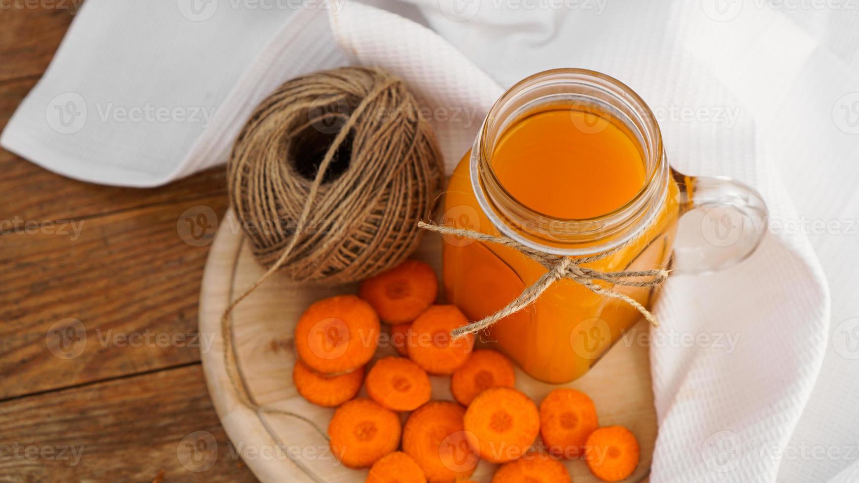 suco de cenoura de laranja brilhante e um novelo de barbante em um fundo de madeira foto
