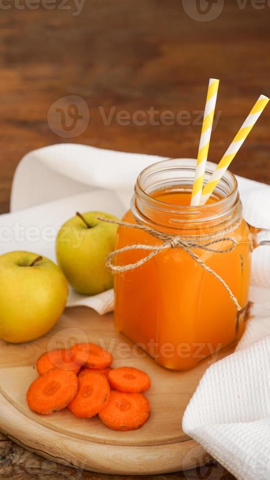 suco de maçã e cenoura em vidro, vegetais frescos e frutas em madeira foto