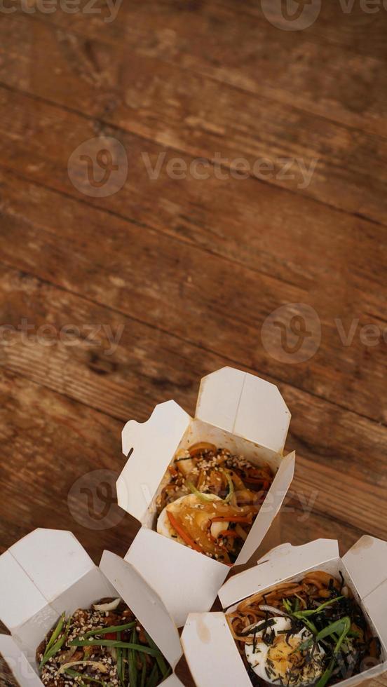 macarrão com carne de porco e vegetais em caixa para viagem na mesa de madeira foto