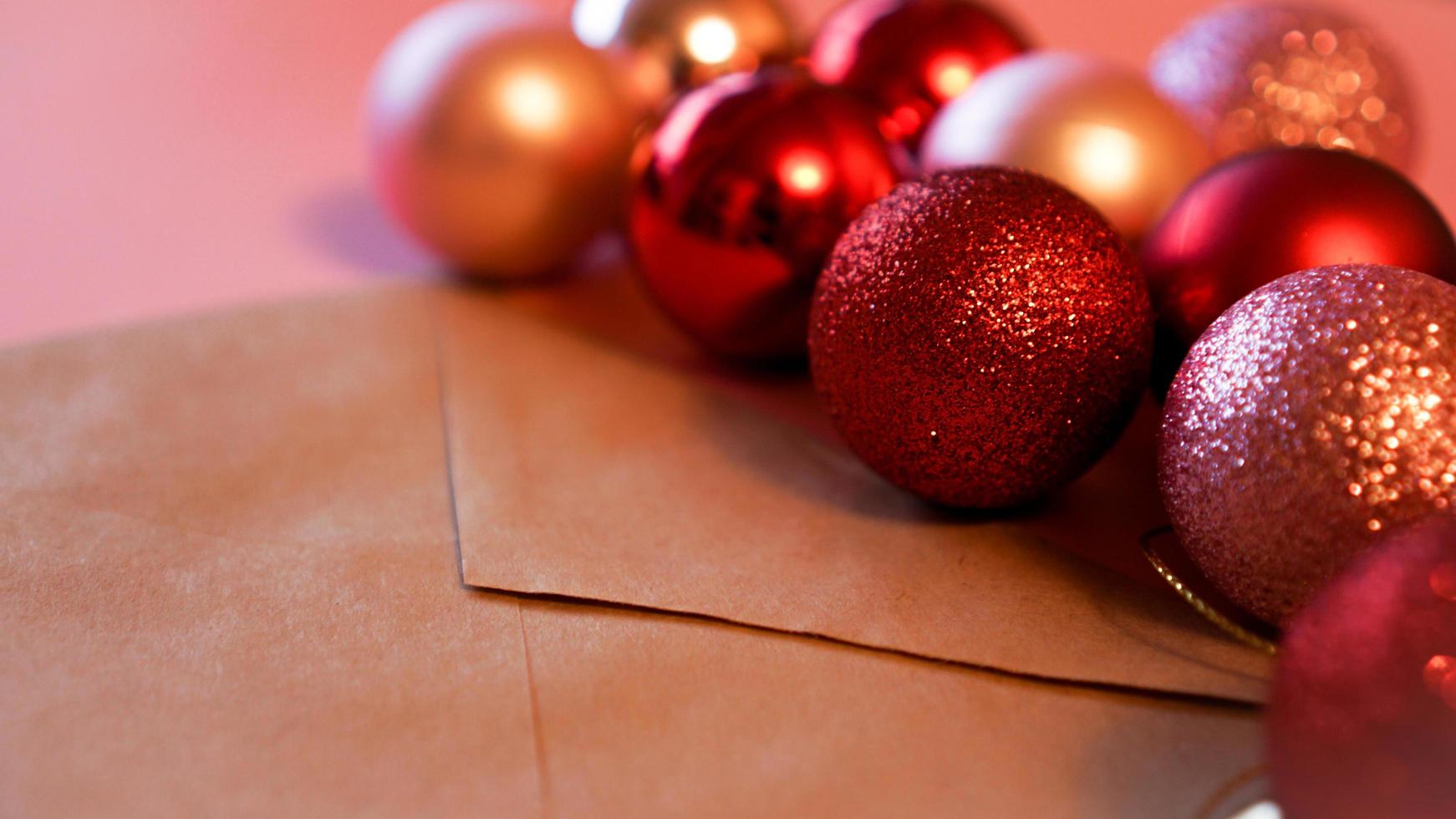 envelope de papel artesanal com bolas vermelhas e rosa de natal em rosa foto