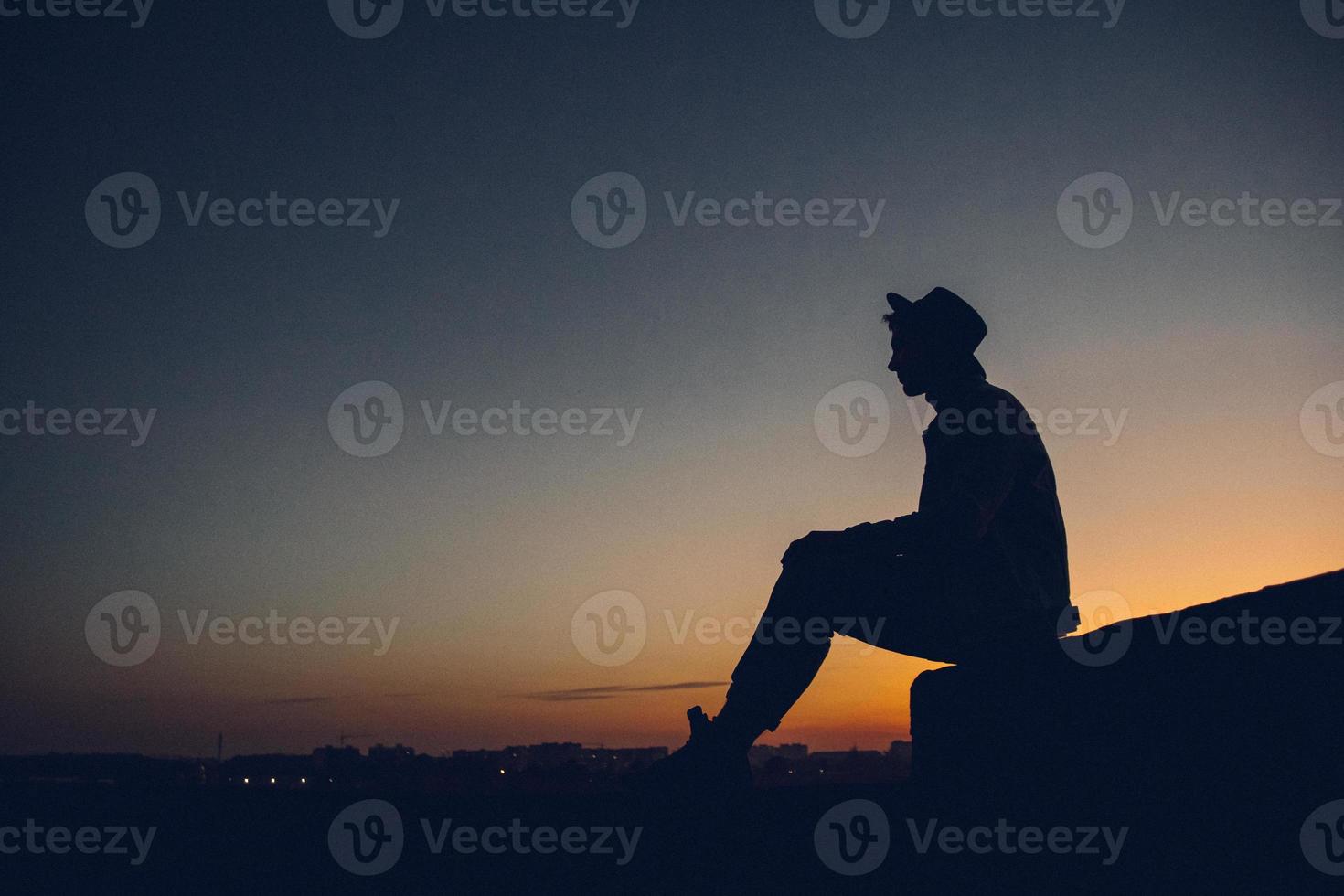 silhueta de um homem observando o pôr do sol sobre a cidade foto