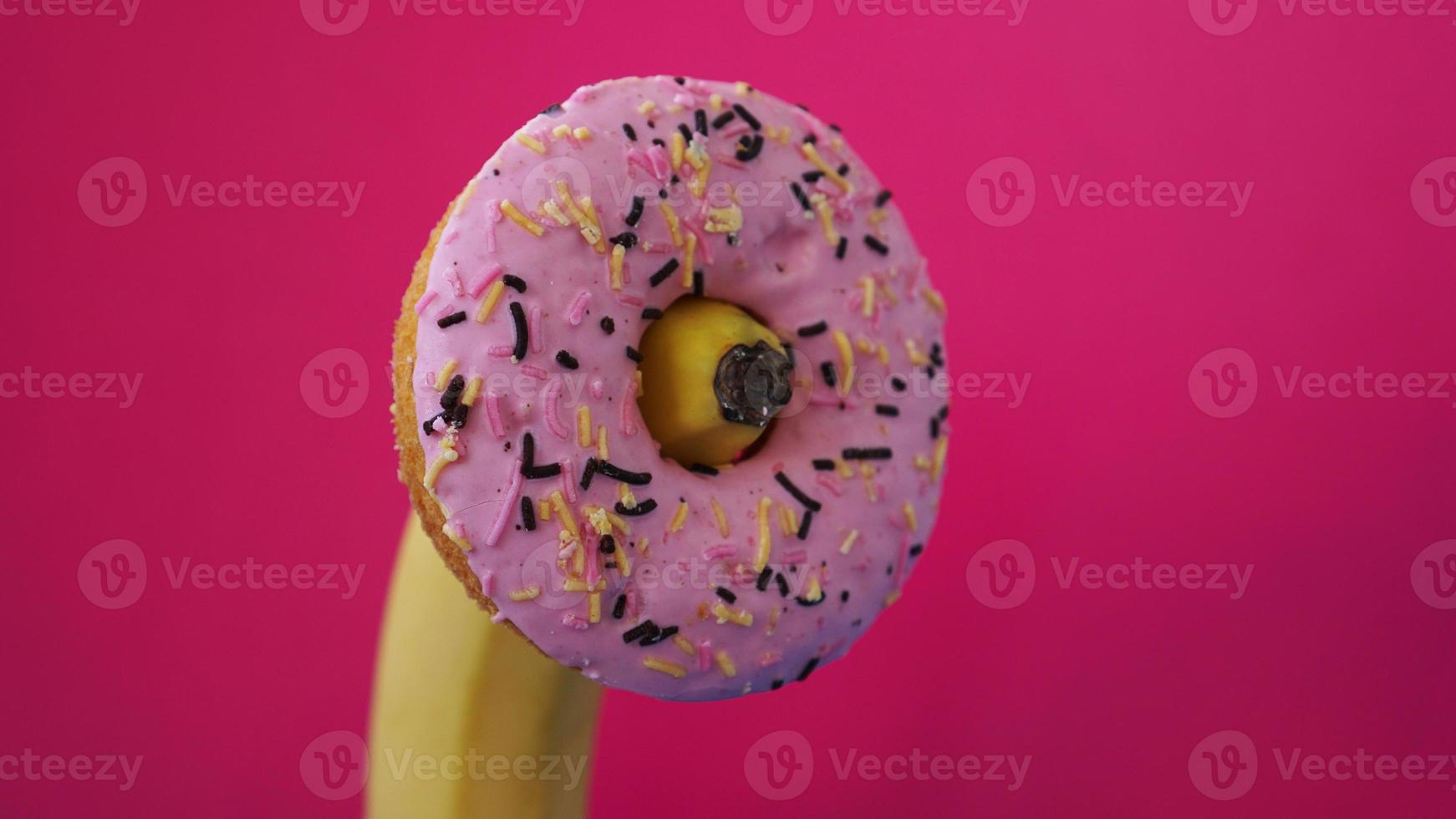 donut doce e banana em fundo de cor rosa. conceito erótico foto