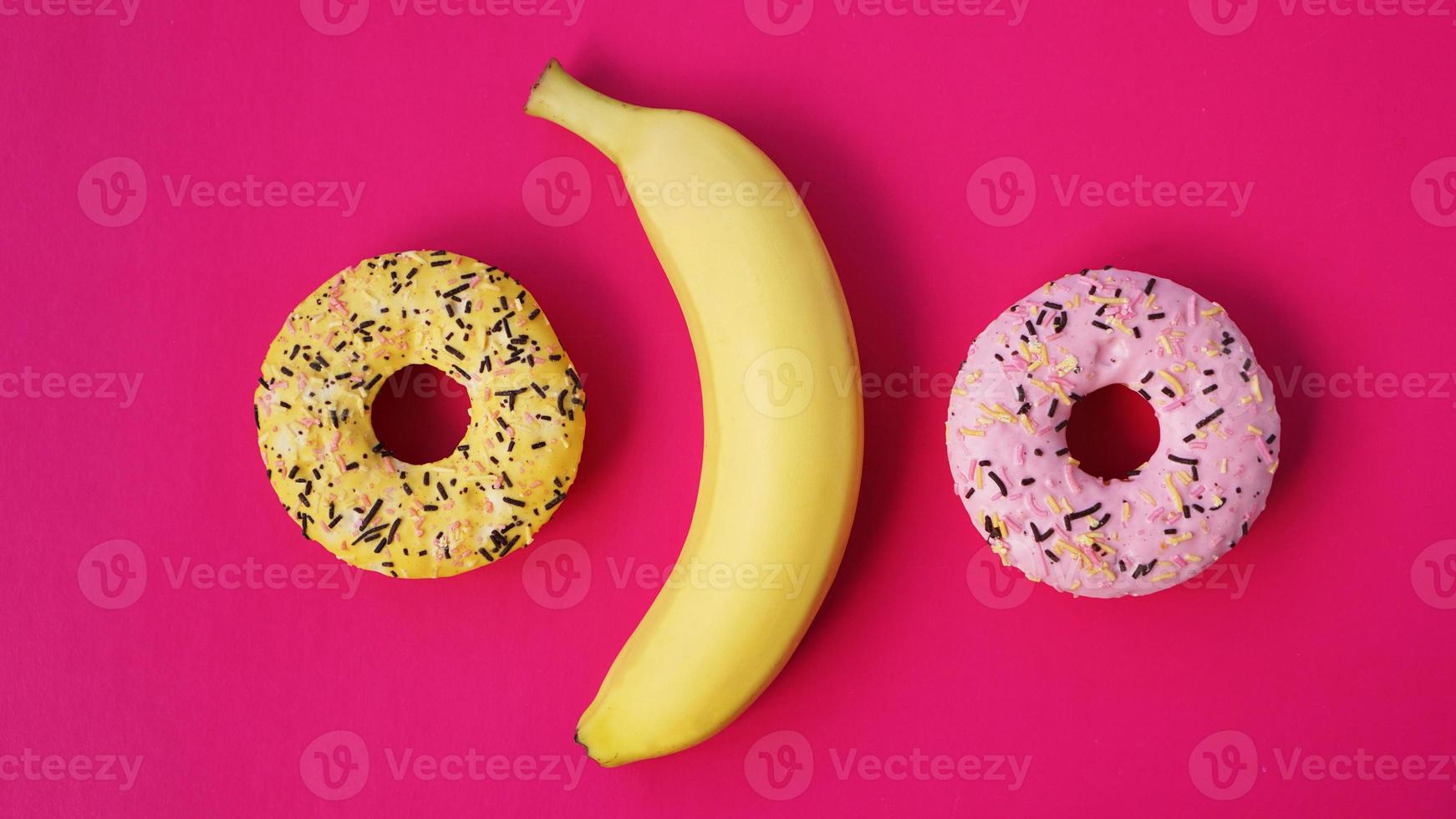 banana amarela e donuts em fundo rosa. vista acima foto