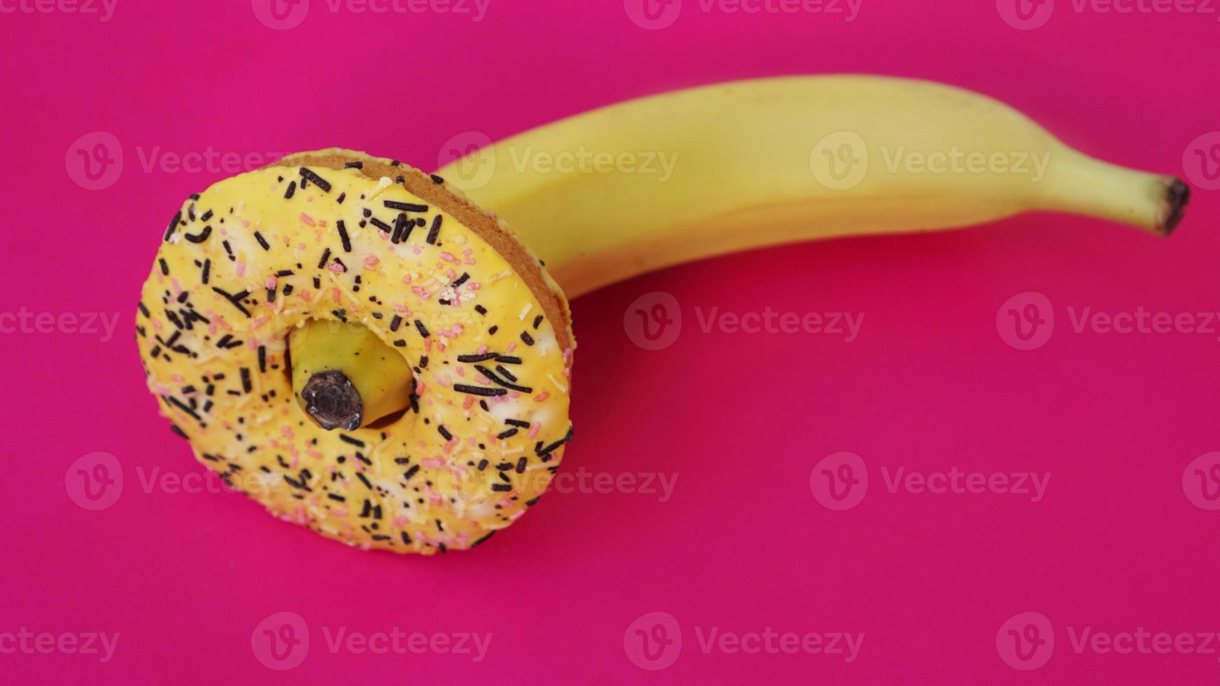 donut doce e banana em fundo de cor rosa. conceito erótico foto