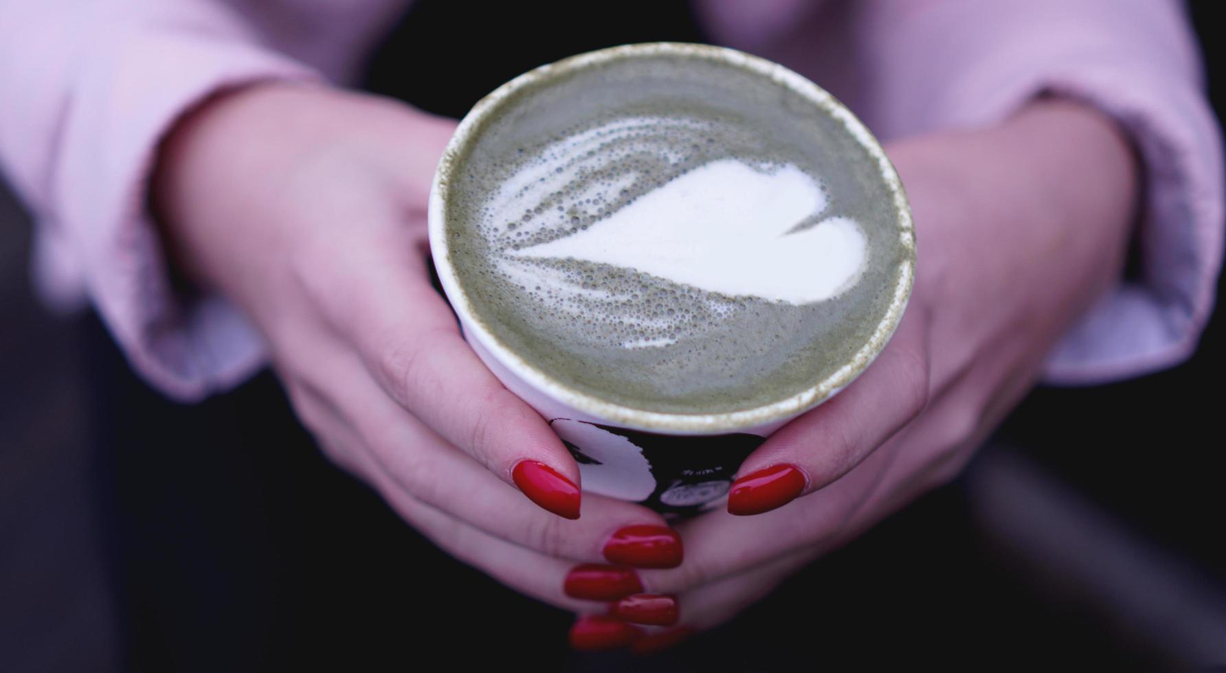 mão feminina segurando chá verde matcha latte quente em copo de papel. foto