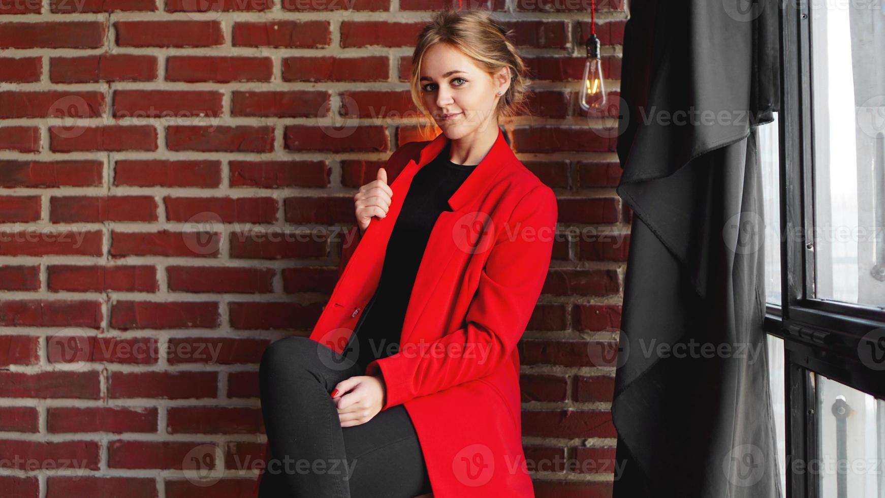 Mulher de negócios feliz e sorriso usando uma jaqueta vermelha sobre a parede de tijolos do escritório foto
