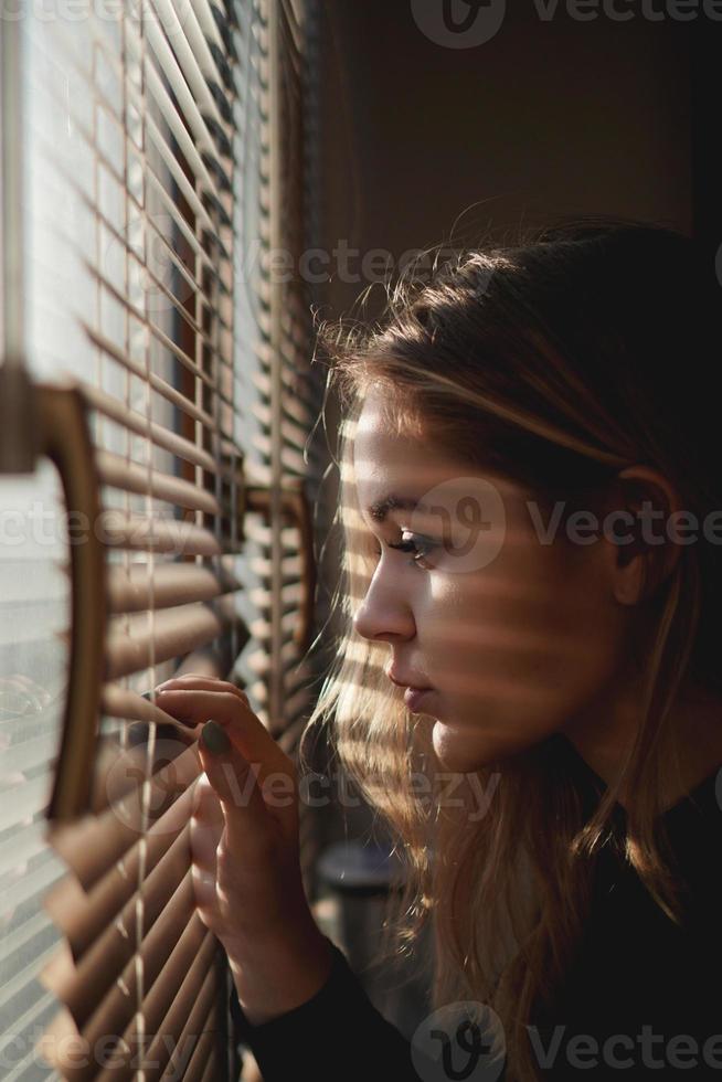 bela jovem olha através das cortinas foto