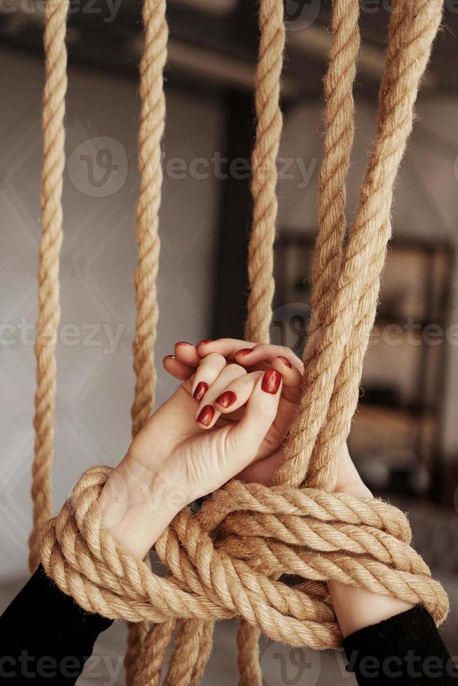 amarrado com uma corda mãos femininas com unhas vermelhas foto