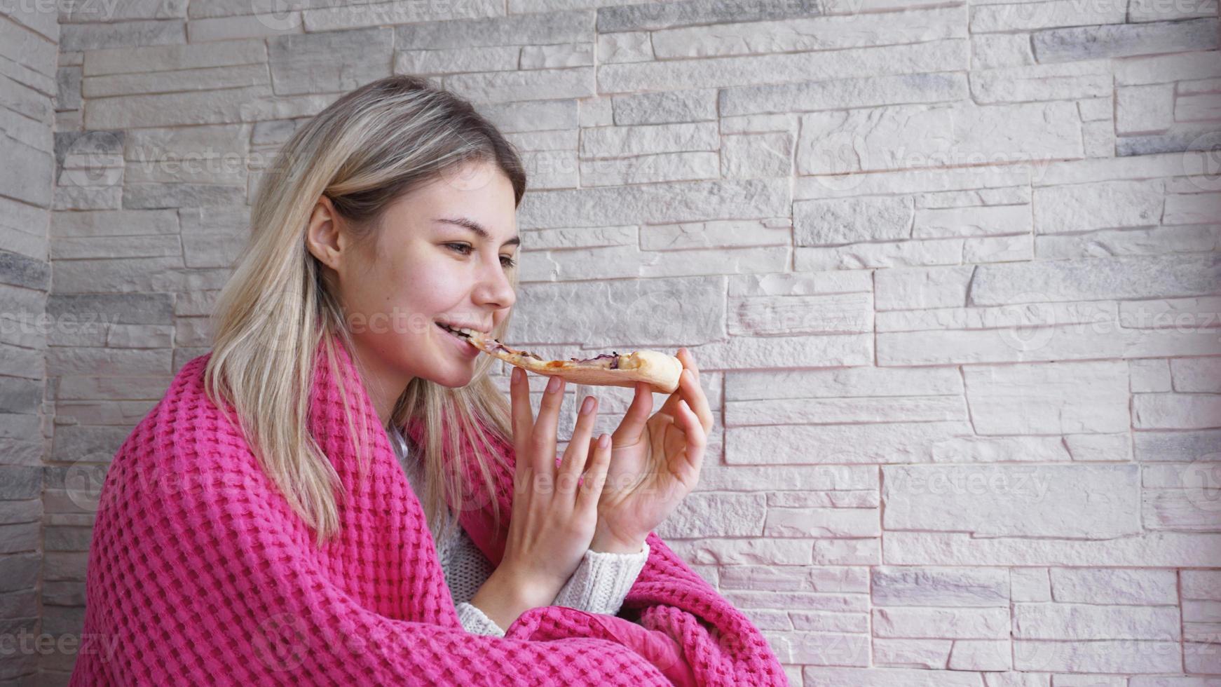 Mulher bonita com manta rosa segurando uma fatia de pizza foto
