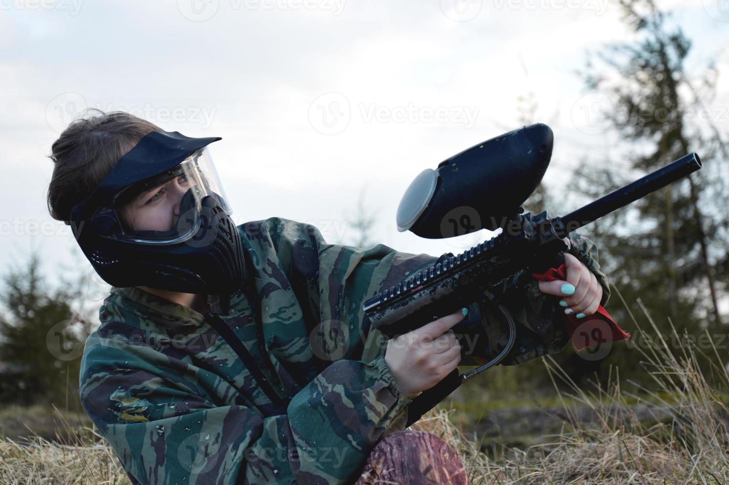 garota jogadora de paintball com uniforme de camuflagem protetora e máscara foto