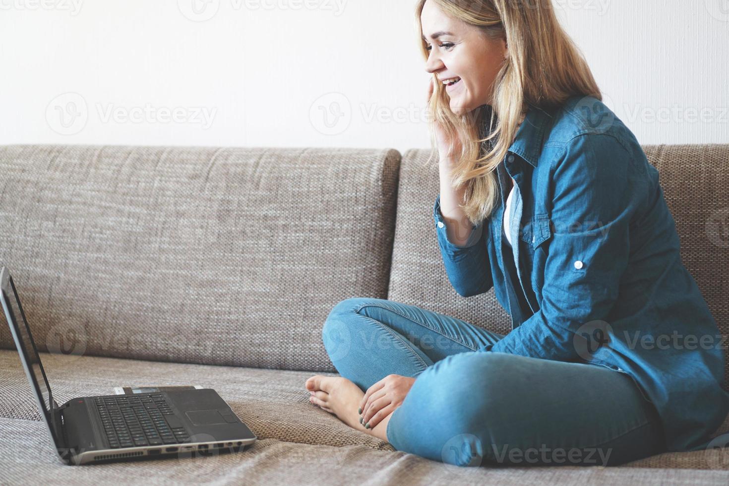 loira sorridente relaxando no sofá com seu laptop foto