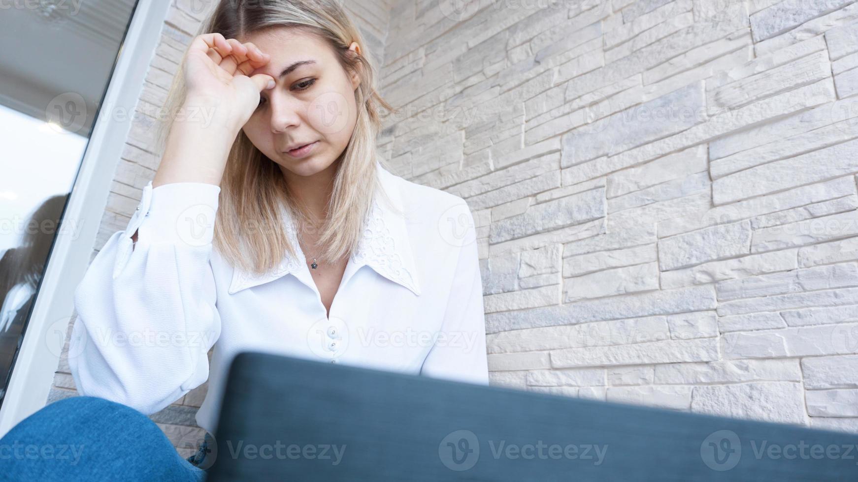 mulher olha para o laptop com uma expressão de preocupação e dor foto