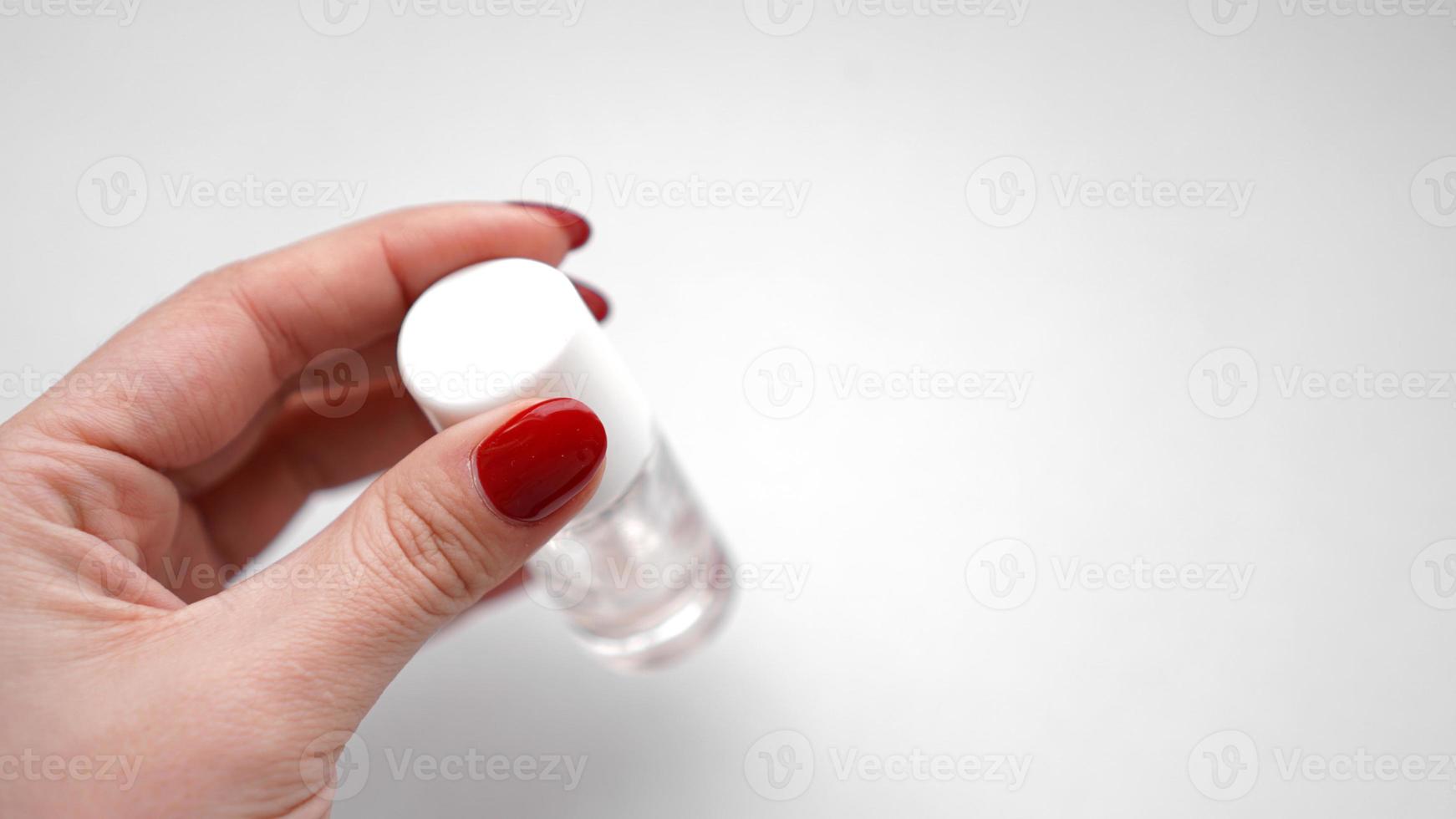 menina com unhas vermelhas segurando esmalte transparente ou óleo de cutícula foto