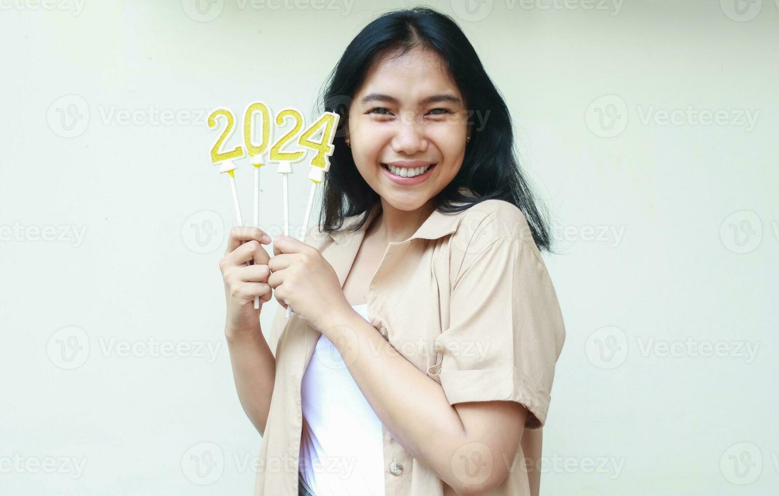 retrato do feliz ásia jovem mulher segurando velas números 2024 com ouro e branco cor sorridente Veja às Câmera cheio do excitação vestindo Castanho camisa isolado foto