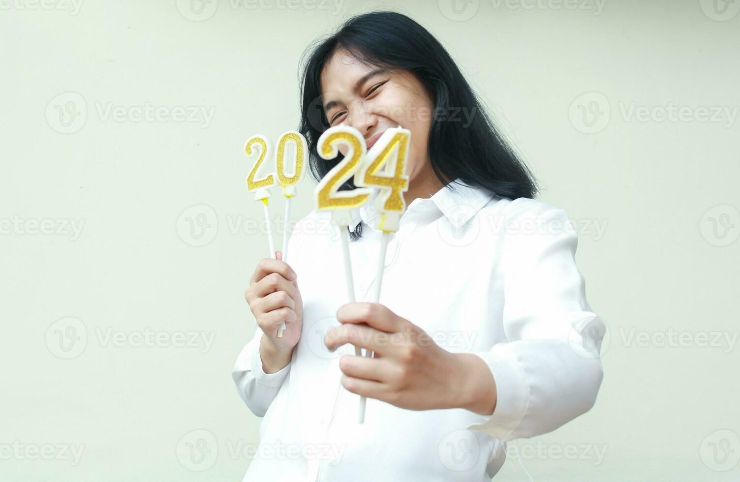 feliz ásia jovem o negócio mulher vestindo branco formal camisa animado para anunciar Novo anos véspera de mostrando número 24 do 2024 número vela aguarde em mão, olhando às Câmera com olho fechado, isolado foto